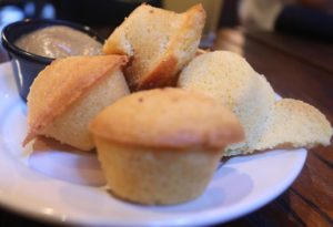 Four cornbread muffins on a plate with honey dipping sauce.