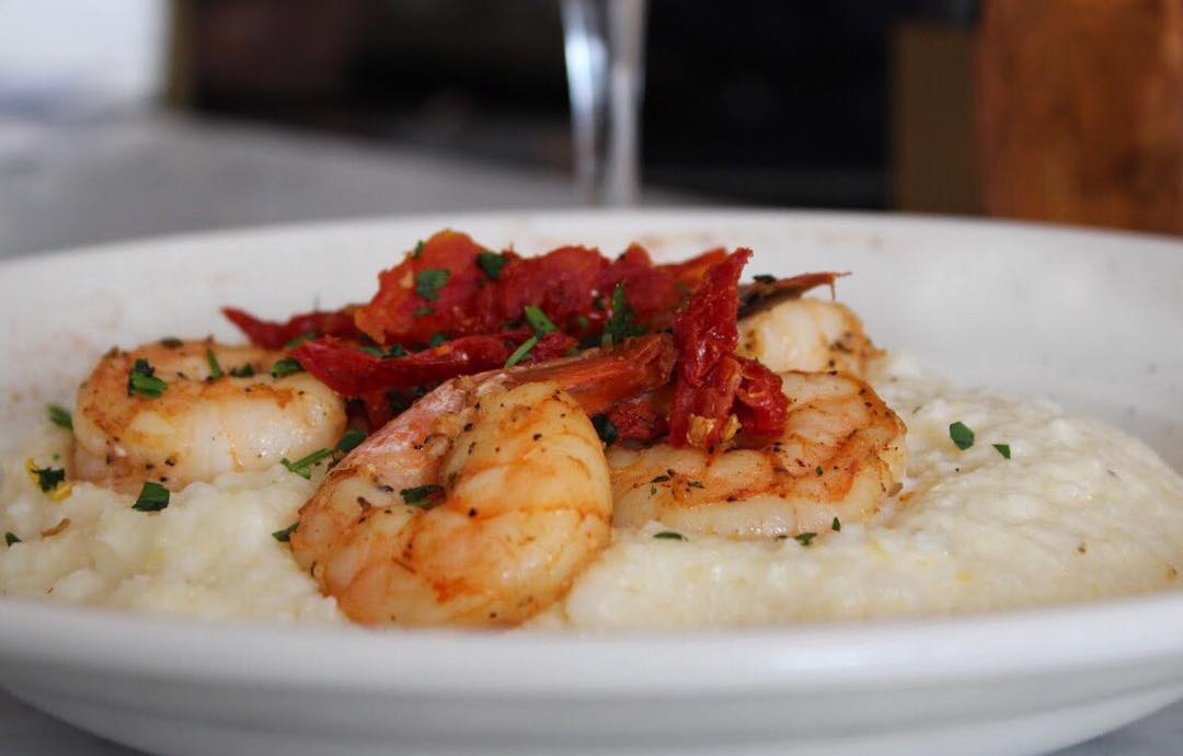 A bowl of girls topped with roasted shrimp and red peppers