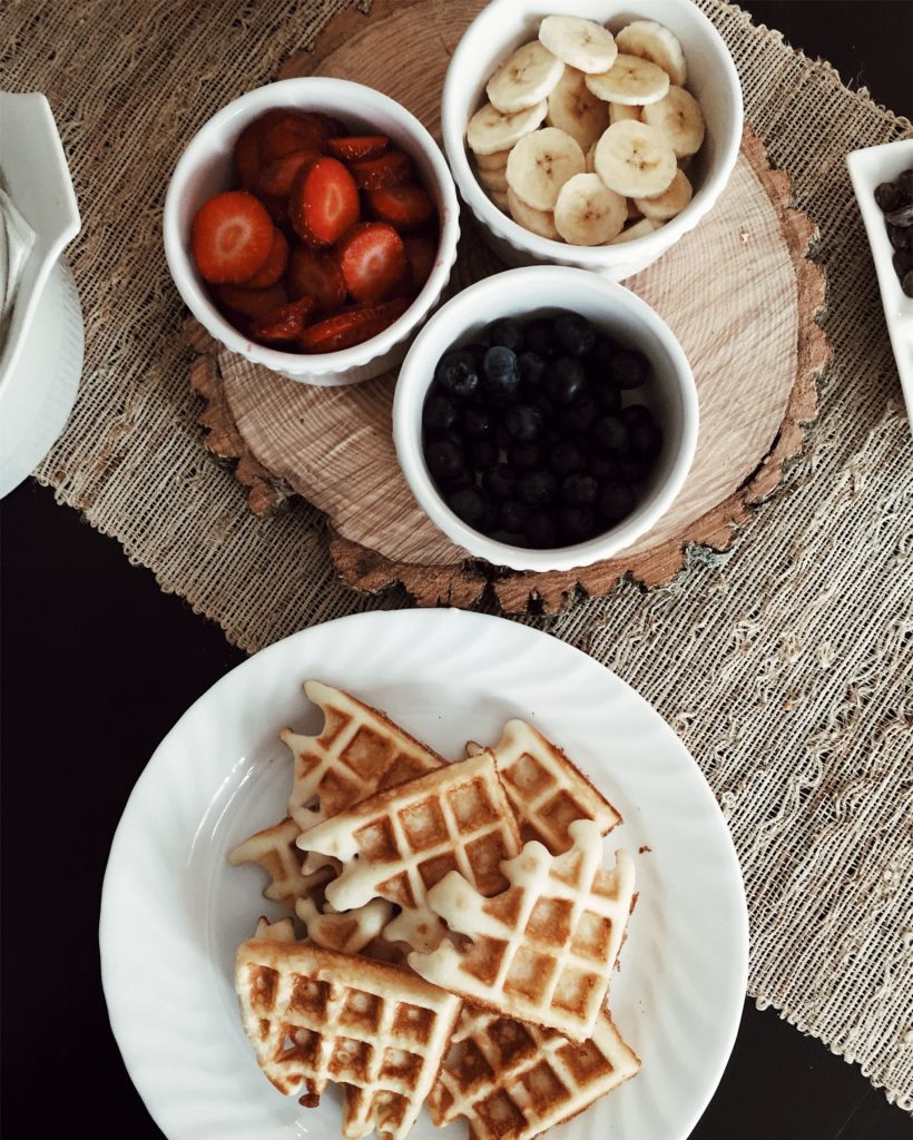 A plate of waffles and bowls of fruit sit on a brunch table. 